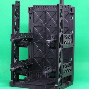 May include: A black, modular diorama set with an industrial design. The set features multiple levels, walkways, and a central wall with an X-shaped pattern. The structure is made of plastic and is designed for miniature figures.