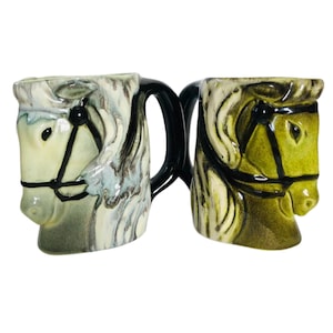 May include: Two ceramic horse head mugs. One mug is green and white, the other is gray and white. Both mugs have black handles and black bridles.