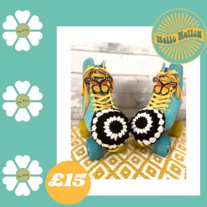 May include: A pair of blue roller skates with black and white crocheted toe covers and butterfly embellishments. The skates are on a yellow and white patterned rug. The text "Hello Mellow" is on a yellow sunburst sticker.