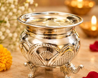 May include: A polished silver-toned metal bowl featuring a wide rim and a rounded body decorated with embossed fan-shaped patterns and beaded borders. The bowl is supported by three legs sculpted in the shape of elephant heads with trunks.