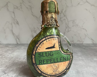 Peut inclure: Une bouteille en verre vert avec un bouchon doré et une étiquette qui indique "Flesh Eating Slug Repellent with Slugs Out Mandrake's Sprout".