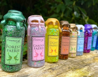 Könnte beinhalten: Eine Reihe dekorativer Glasflaschen, gefüllt mit Glitzer und bunten Flüssigkeiten. Jede Flasche hat ein Etikett mit der Aufschrift "Essence of", gefolgt von einem Thema wie "Forest Faerie". Die Flaschen sind mit Wachs versiegelt.