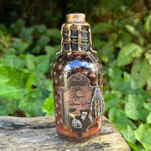 May include: A small glass bottle with a gold metal top and a black chain. The bottle is filled with a dark liquid and has a label that reads 'Gin Reaper's Captured Souls'. A silver skeleton hand charm hangs from the chain.