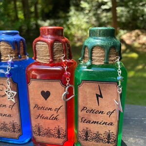 May include: Three glass potion bottles with cork stoppers and labels. The bottles are filled with blue, red, and green liquid. The labels read "Potion of Mana", "Potion of Health", and "Potion of Stamina".