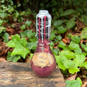 May include: A small glass bottle with a silver and red wax seal. The bottle is filled with a dark purple liquid and has a label that reads "Elixir of Chaos".