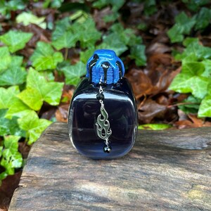 May include: A small, dark blue glass bottle with a black and blue dripping top. The bottle has a silver charm hanging from it, shaped like a flame.