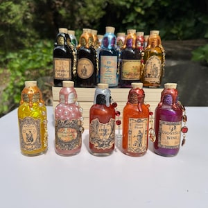 May include: A selection of decorative potion bottles with cork stoppers. The bottles are decorated with labels and colourful drippings, including gold, pink, red, and purple. Some bottles have beaded accents. The labels feature text and illustrations.