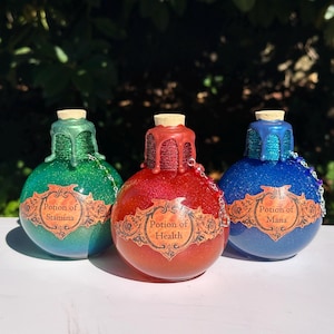May include: Three glittery potion bottles in green, red, and blue, each with a cork stopper and a decorative label. The labels read "Potion of Stamina", "Potion of Health", and "Potion of Mana". Each bottle has a chain.