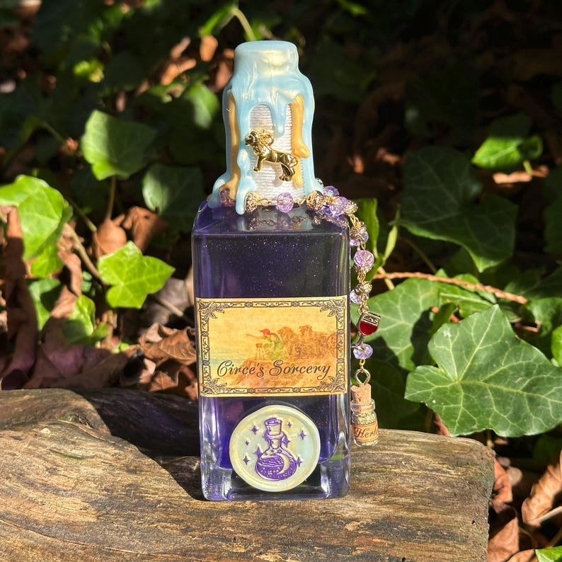 May include: A glass bottle with a blue and gold wax seal on the top. The bottle contains a purple liquid and has a label that reads "Circe's Sorcery". The bottle is decorated with a gold charm and a beaded chain.