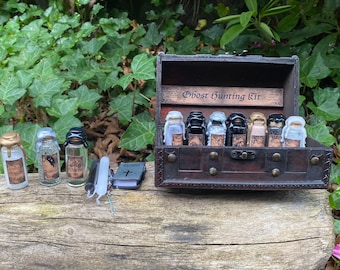May include: A wooden chest labeled "Ghost Hunting Kit" with a variety of small glass bottles containing liquids. The bottles are labeled with names like "White Sage", "Border Song", and "Dark Whisper".
