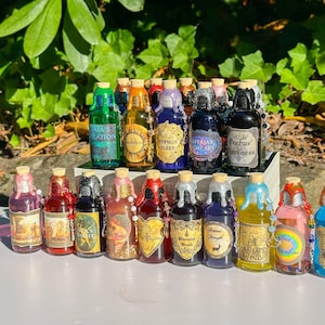 May include: A collection of small, decorative glass bottles with cork stoppers. Each bottle has a unique label and is filled with a colorful liquid. Some bottles have decorative wax seals and beaded accents. The labels feature various text, including "Gaia's Creation" and "Erebus Darkness".