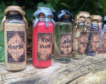 Può includere: Sei piccole bottiglie di vetro con tappi di sughero ed etichette. Le bottiglie contengono vari ingredienti, tra cui aglio, un liquido rosso etichettato "The Cure for Vampirism", un liquido trasparente etichettato "Holy Water", erbe, cristalli blu e una polvere bianca. Le bottiglie sono disposte in fila su una superficie di legno.