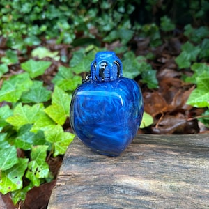 May include: A small, blue, heart-shaped bottle with a black and blue stopper. The bottle has a swirling, marbled effect.