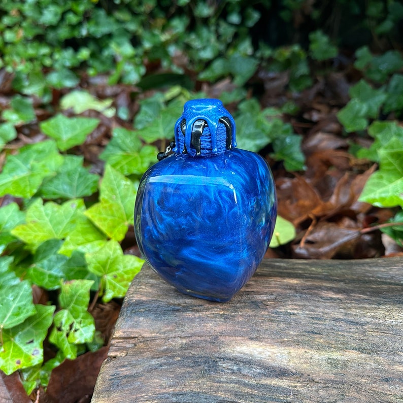 May include: A small, blue, heart-shaped bottle with a black and blue stopper. The bottle has a swirling, marbled effect.
