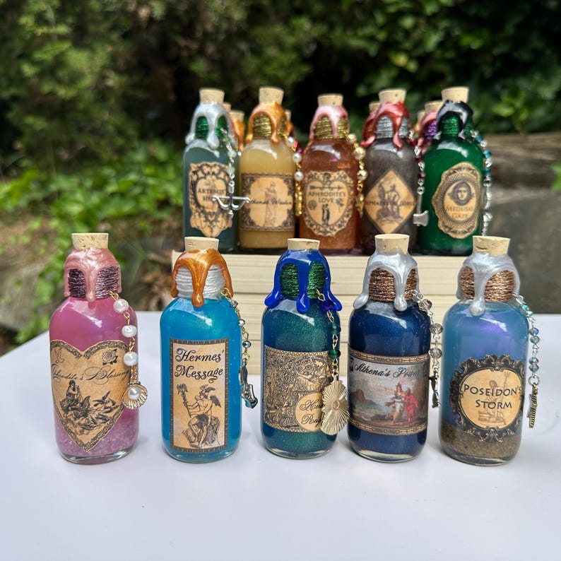May include: A selection of decorative potion bottles with cork stoppers and colourful liquid contents. Each bottle has a unique label and is adorned with decorative elements like beads and charms. The bottles are arranged in front of a blurred green background.