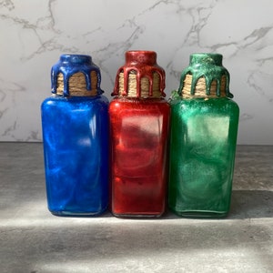 May include: Three glass bottles with glitter inside. The bottles are blue, red, and green. Each bottle has a brown twine tied around the top and a wax seal.