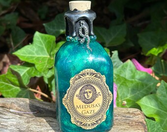 May include: A small green glass bottle with a black wax seal and a silver snake charm. The bottle has a gold label with the text "Medusa's Gaze".