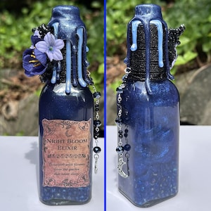 May include: A dark blue glass bottle labelled "Night Bloom Elixir." It features blue floral decorations, dripping blue wax, and a beaded chain with a crescent moon charm. The bottle's contents shimmer with blue glitter, creating a magical aesthetic.