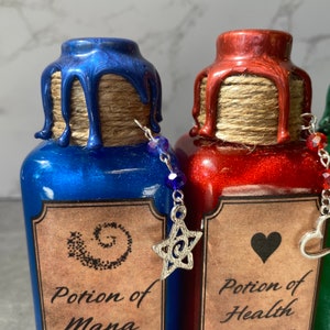 May include: Three glass potion bottles with cork stoppers and labels. The bottles are filled with blue, red, and green glitter. The labels read "Potion of Mana", "Potion of Health", and "Potion of Strength". Each bottle has a charm attached to the cork.