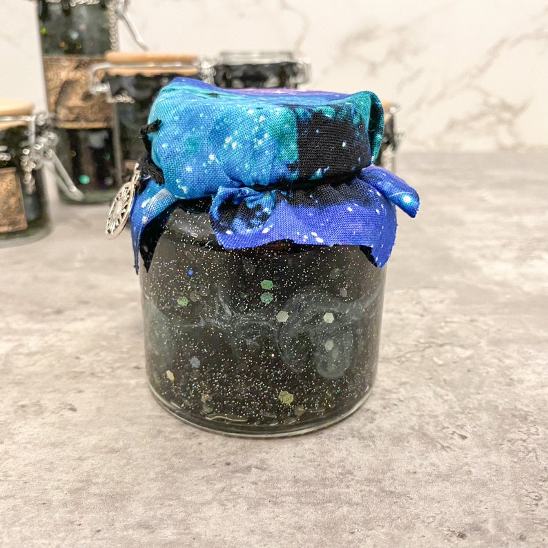 May include: A glass jar filled with black glitter and a swirling blue and green pattern, topped with a blue and black fabric lid.