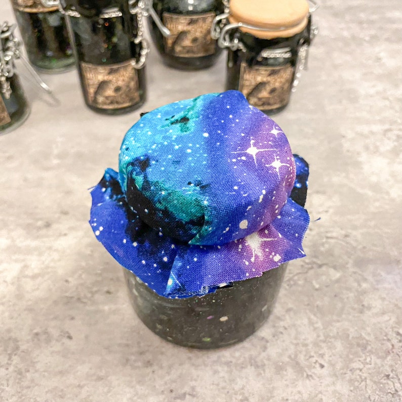 May include: A glass jar with a galaxy print fabric lid. The fabric is blue, purple, and black with white stars.