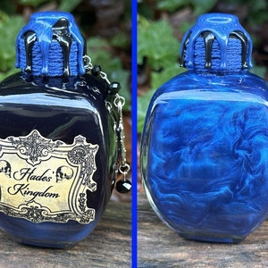 May include: A dark blue glass bottle with a black and blue stopper. The bottle has a gold label that reads "Hades' Kingdom".