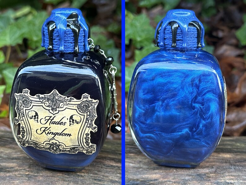 May include: A dark blue glass bottle with a black and blue stopper. The bottle has a gold label that reads "Hades' Kingdom".
