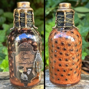 May include: A small glass bottle with a gold and black stopper and a label that reads "Grim Reaper's Captured Soul". The bottle is filled with a brown liquid and has a black and gold design.