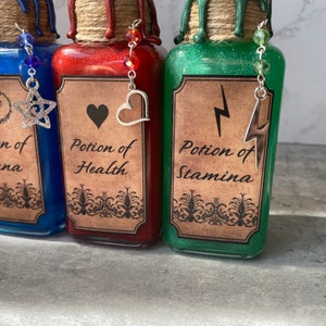 May include: Three glass bottles with cork stoppers and labels. The bottles are filled with blue, red, and green liquids. The labels read "Potion of Stamina", "Potion of Health", and "Potion of Strength".