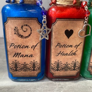 May include: Three small glass bottles with cork stoppers and decorative charms. The bottles are filled with blue, red, and green liquids. The labels on the bottles read "Potion of Mana", "Potion of Health", and "Potion of Strength".