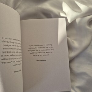 May include: A white book with a quote from Marcus Aurelius about pain and distress. The quote reads: "If you are distressed by anything external, the pain is not due to the thing itself, but to your estimate of it; and this you have the power to revoke at any moment."