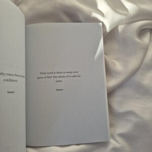 May include: An open book with a white background. The text on the page reads: "What need is there to weep over parts of life? The whole of it calls for tears. Seneca"
