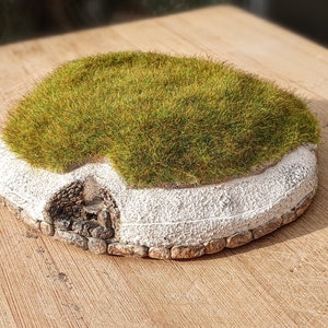 May include: A miniature model of a grass-covered stone hut with a white plaster wall and a stone entrance.