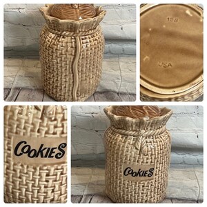Puede incluir: Una jarra de galletas de cerámica marrón con forma de saco de arpillera con la palabra "COOKIES" escrita en la parte delantera. La tapa tiene una textura tejida y la parte inferior de la jarra tiene el número "158" y "USA" impresos.