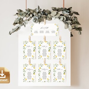May include: Lemon themed wedding table seating chart with a white background and green eucalyptus leaves hanging from the top. The chart is made up of 8 cards with the text "Table One", "Table Two", "Table Three", "Table Four", "Table Five", "Table Six", "Table Seven", and "Table Eight" printed on each card. Each card features a watercolour illustration of lemons and leaves.