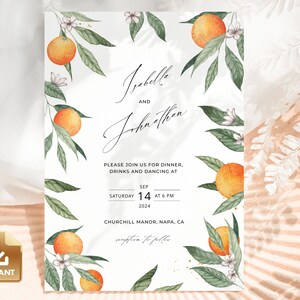 May include: A white wedding invitation with a floral design featuring orange blossoms and oranges. The invitation reads "Isabella and Johnathan" and includes the date, time, and location of the wedding.