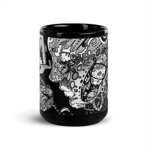 May include: Black ceramic mug with a white and black graphic design of a face with intricate details. The design features a stylized face with geometric patterns and swirls.