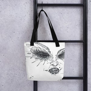May include: A white tote bag with a black and white illustration of a face with large eyes and a bold lip. The illustration is in a graphic style and has a slightly abstract feel.