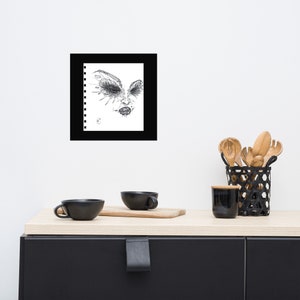 May include: Black and white drawing of a face with intricate details around the eyes, framed in a black frame.