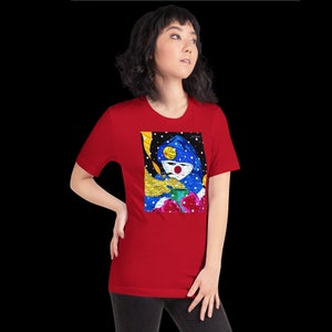 May include: Red short-sleeved t-shirt with a colorful graphic print of a person wearing a blue hooded jacket and holding a green cup. The graphic also includes a yellow hand, red roses, and a black background with white snowflakes.