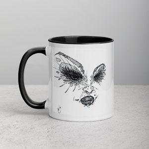 May include: White ceramic mug with a black rim and handle. The mug features a black and white line drawing of a face with dramatic eyelashes and lips.