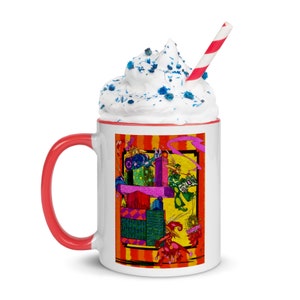 May include: White ceramic mug with a red rim and handle. The mug features a colorful illustration of a whimsical scene with geometric shapes and figures. The mug is filled with whipped cream and blue sprinkles, topped with a red and white striped straw.