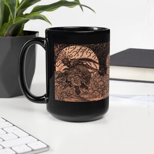Könnte beinhalten: Schwarze Keramiktasse mit weißem Henkel. Die Tasse zeigt eine Schwarzweißillustration eines geflügelten Wesens vor dem Hintergrund eines Vollmonds. Die Illustration ist in Sepiatönen gehalten.