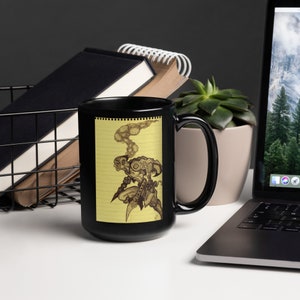 Può includere: Tazza in ceramica nera con sfondo giallo e un'illustrazione in bianco e nero di un robot con fumo che esce dalla testa. L'illustrazione è su uno sfondo di blocco note con righe.