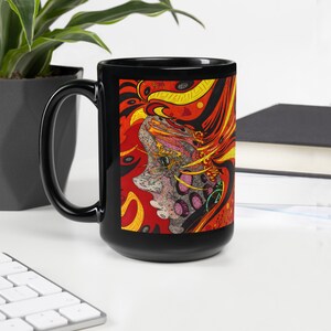 May include: Black ceramic mug with a colorful abstract design featuring a face with red, yellow, orange, and black colors. The design is reminiscent of a psychedelic art style.