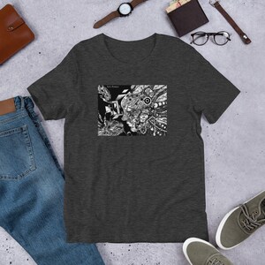 May include: A dark heather grey t-shirt with a black and white graphic print of a face with intricate details. The text "Rob Potter" is printed in the top left corner of the graphic.