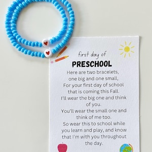 May include: Two blue beaded bracelets with white heart charms and a card with the text "first day of PRESCHOOL" and a message about wearing the bracelets on the first day of school.