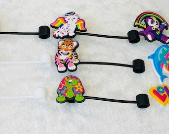 May include: Set of eight colorful phone charms featuring various cartoon characters and designs, including a unicorn, a turtle, a dolphin, a tiger, a cat, aliens in a car, and a panda bear. The charms are attached to black and white cords.
