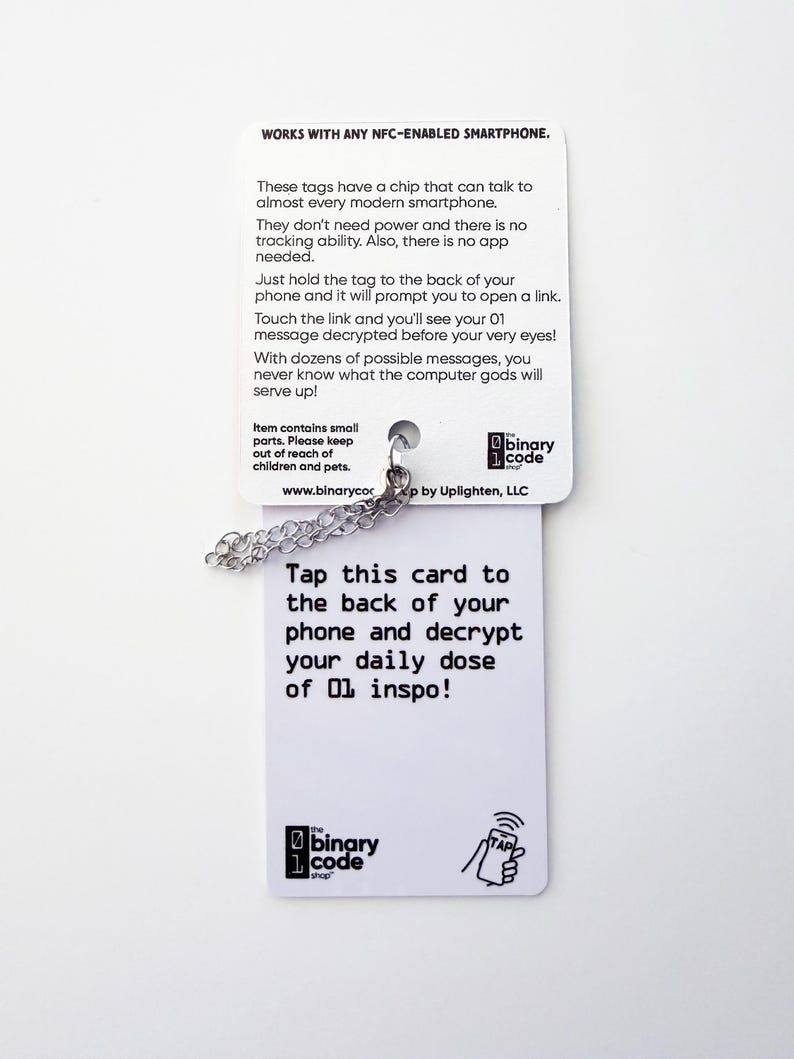Peut inclure: Une &eacute;tiquette rectangulaire blanche compatible NFC avec une cha&icirc;ne en m&eacute;tal argent&eacute;. La carte comporte du texte noir incluant les instructions : Works with any NFC-enabled smartphone. Tap this card to the back of your phone and decrypt your daily dose of 01 inspo!