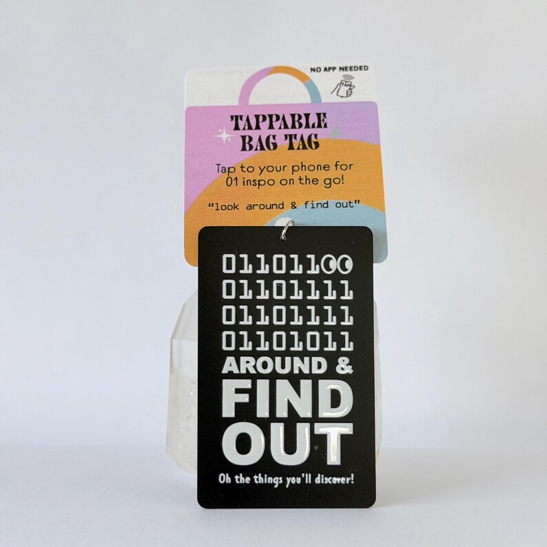 Peut inclure: Une &eacute;tiquette de sac rectangulaire noire avec un code binaire blanc et le texte AROUND & FIND OUT. Elle est fix&eacute;e &agrave; une carte de pr&eacute;sentation color&eacute;e portant le texte TAPPABLE BAG TAG, Tap to your phone for 01 inspo on the go!, look around & find out, et Oh the things you'll discover!